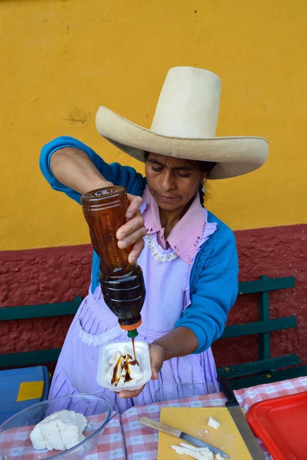 A countrywoman in Cajamarca pouring dark cane syrup, the miel poured over fresh quesillo