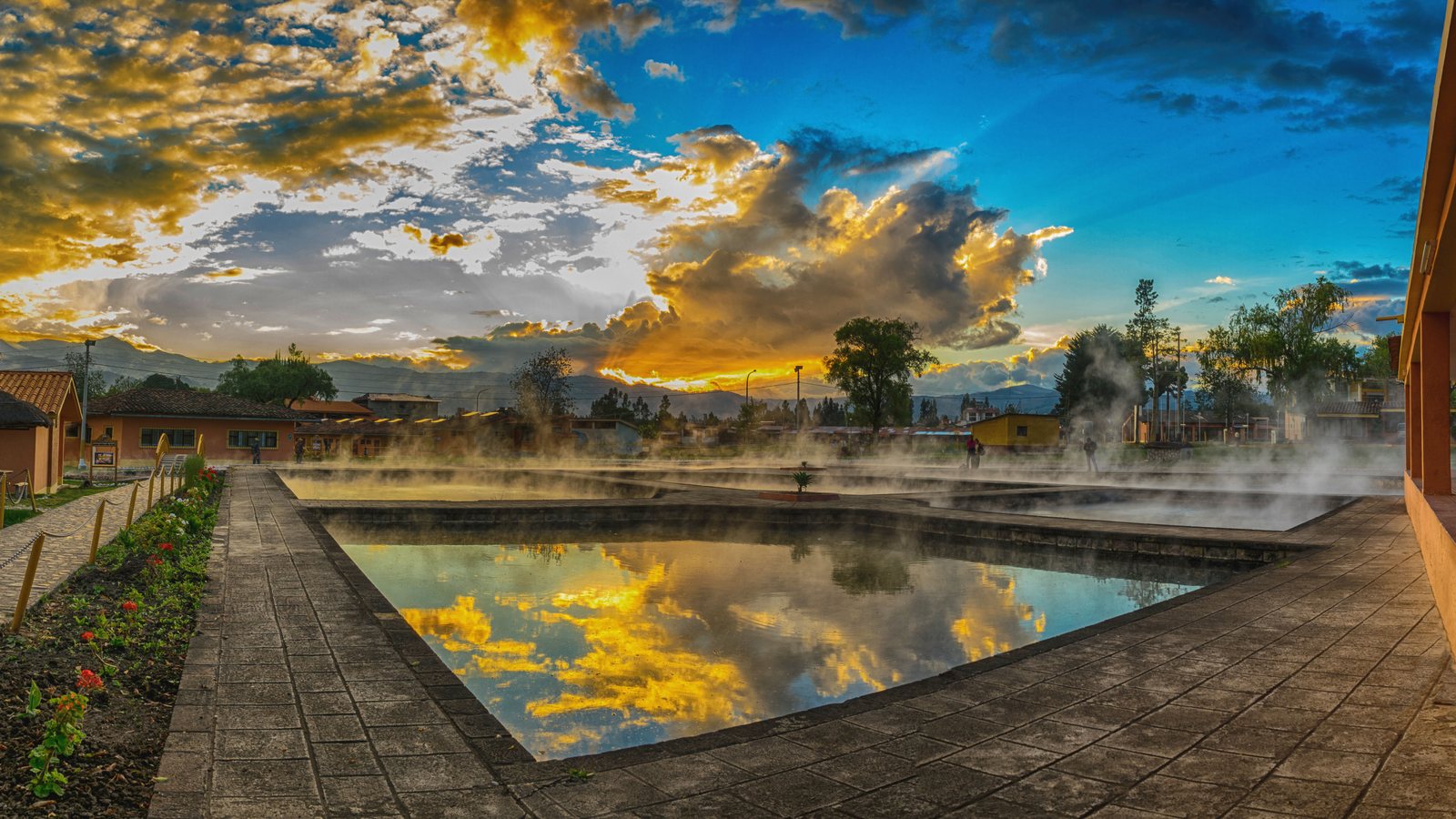 The thermal pools at Baños del Inca at sunset, steam lifting off water that mirrors a gold and blue sky