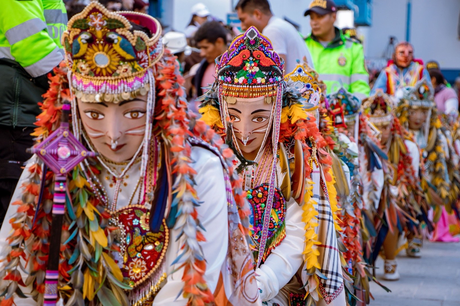 Carnival dancers in beaded masks and headdresses of orange and green feathers, close together in a parade