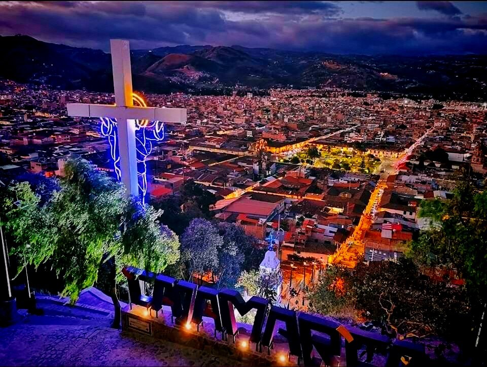 Cajamarca lit up at dusk seen from Santa Apolonia, the hilltop cross in the foreground